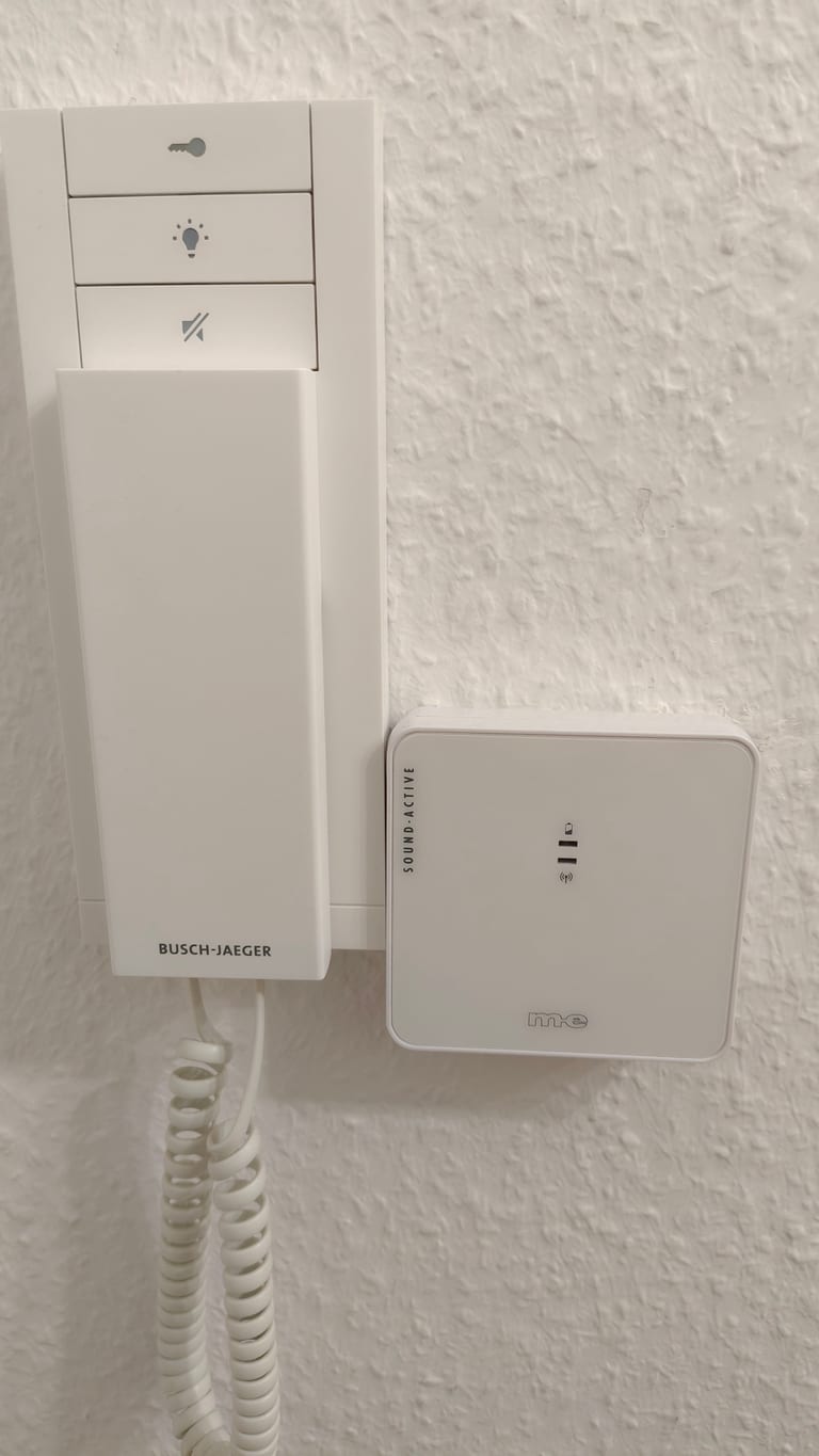 A Busch-Jaeger intercom handset on the wall with a white m-e Sound-Active box mounted above it.