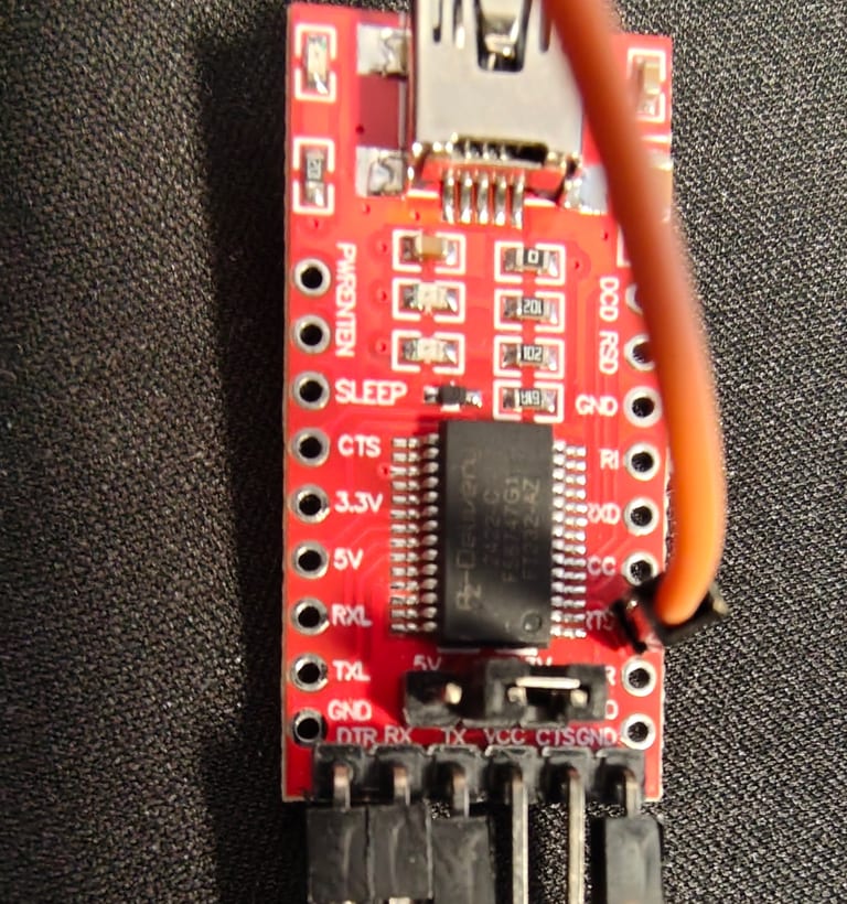 A red FT232RL USB-to-serial adapter with an orange jumper wire soldered to the RTS pad.